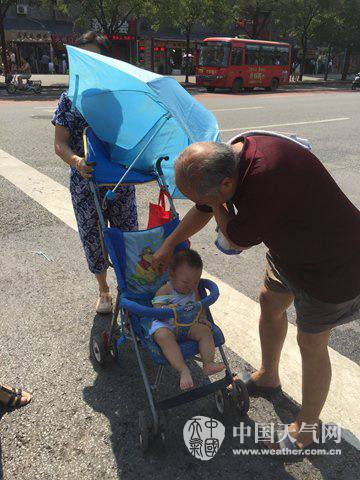 7月31日，西安街头两位老人为孩子遮阳防晒。（张宏芳 摄）